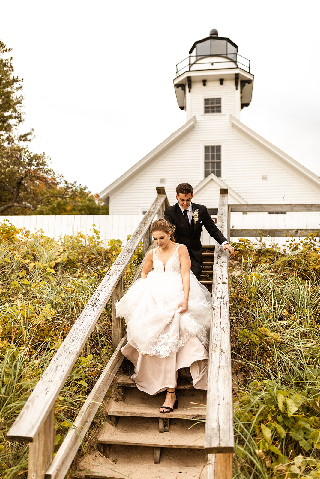 bride and groom wedding photos walking down beach stairway at lighthouse in Michigan