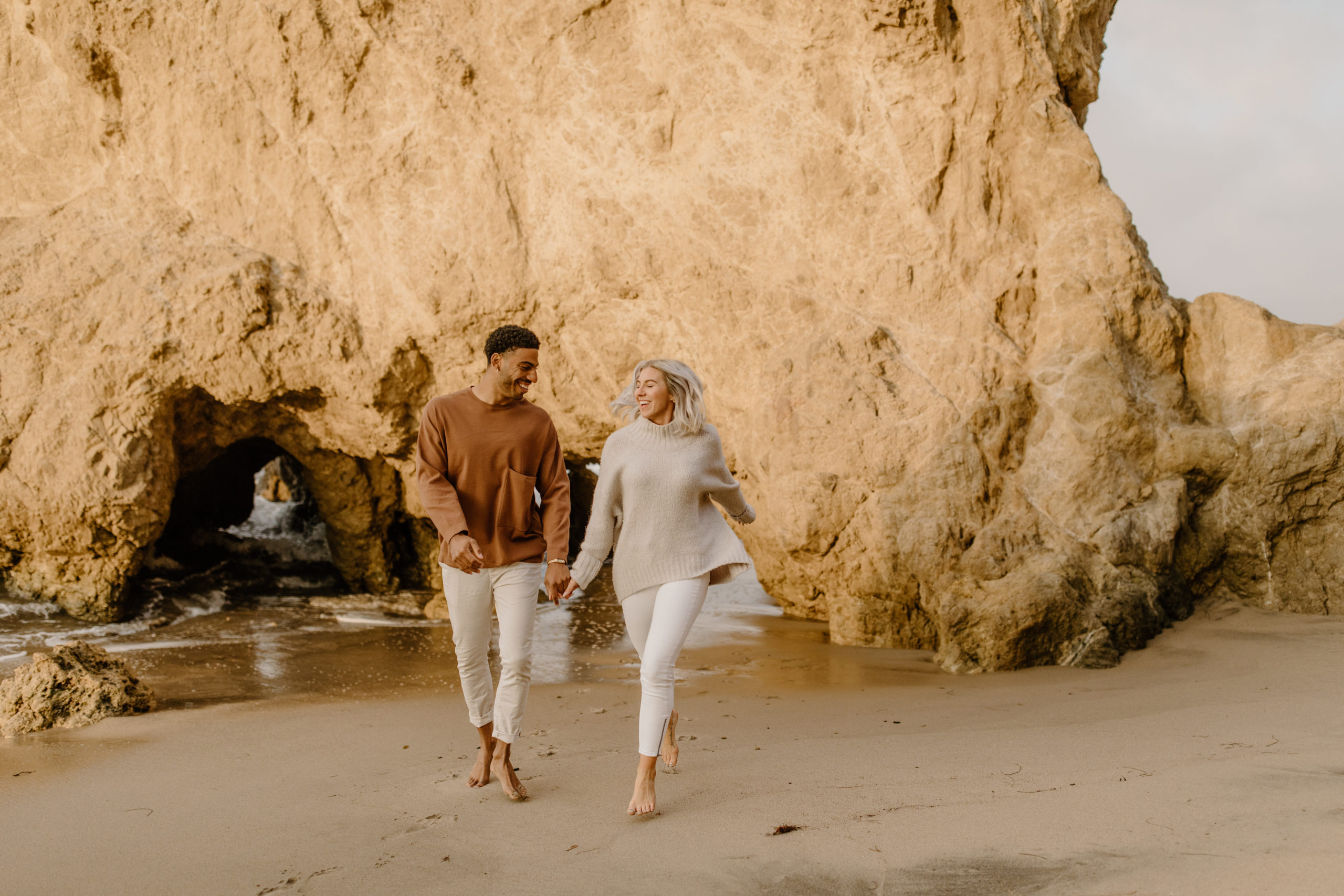 couple holding hands and running at california beach engagement session