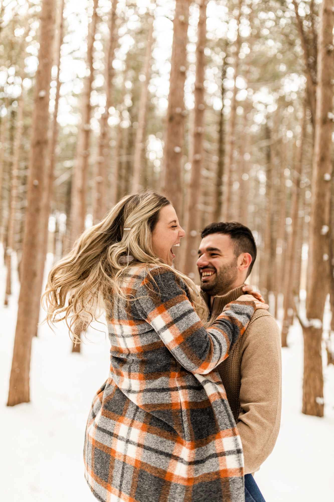 couple laughing in fun snowy winter engagement photos in Michigan forest 