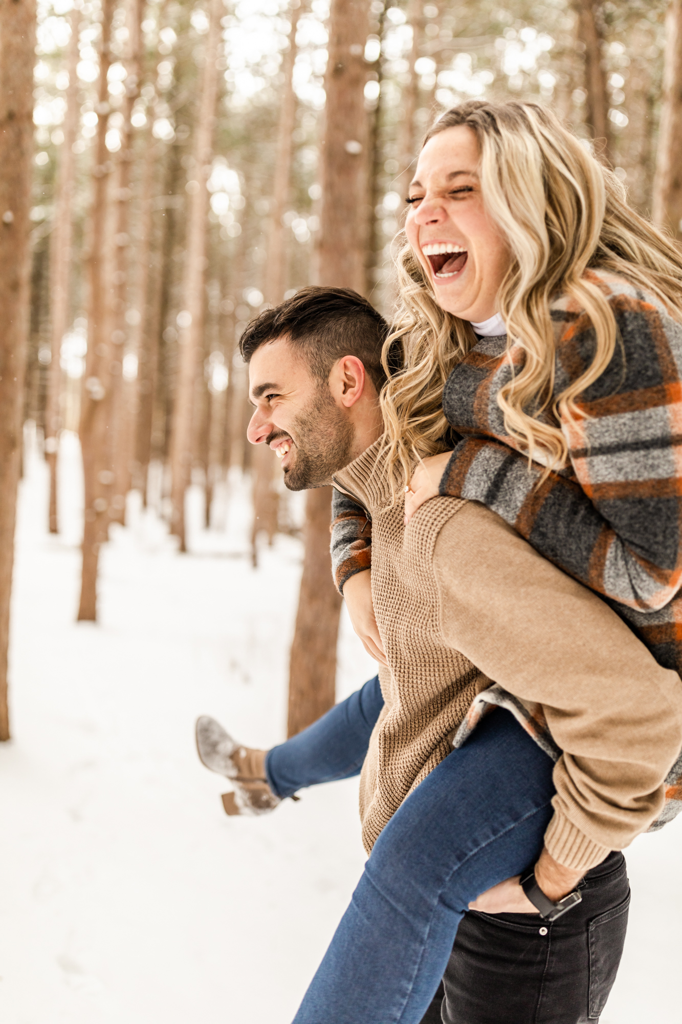 Man carrying woman on his back and laughing in winter snowy engagement photo session