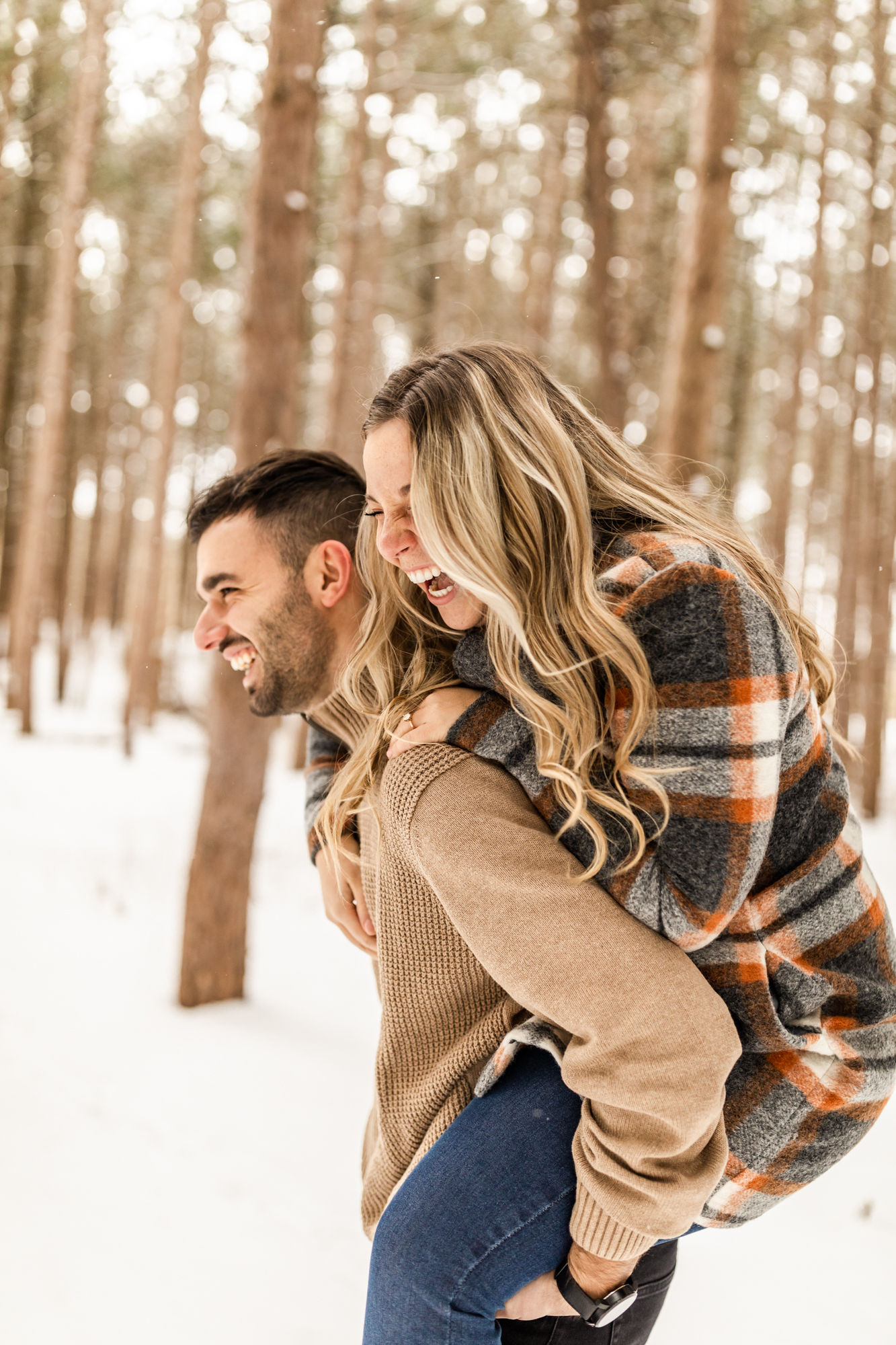 Man carrying woman on his back and laughing in snowy forest in Michigan