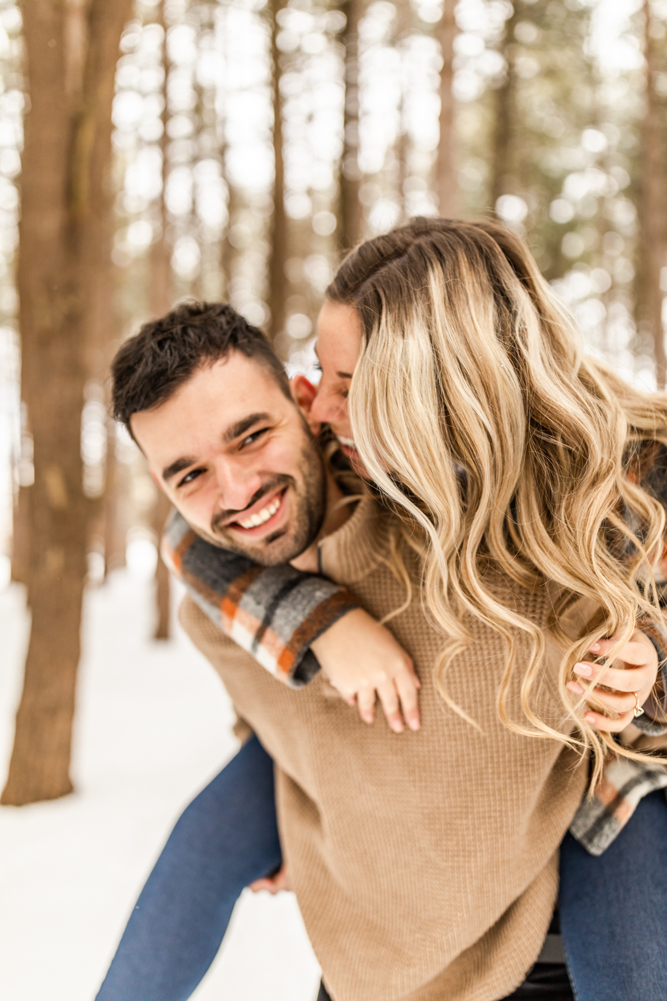 Man carrying woman on his back and smiling in candid engagement photos in winter snowy forest