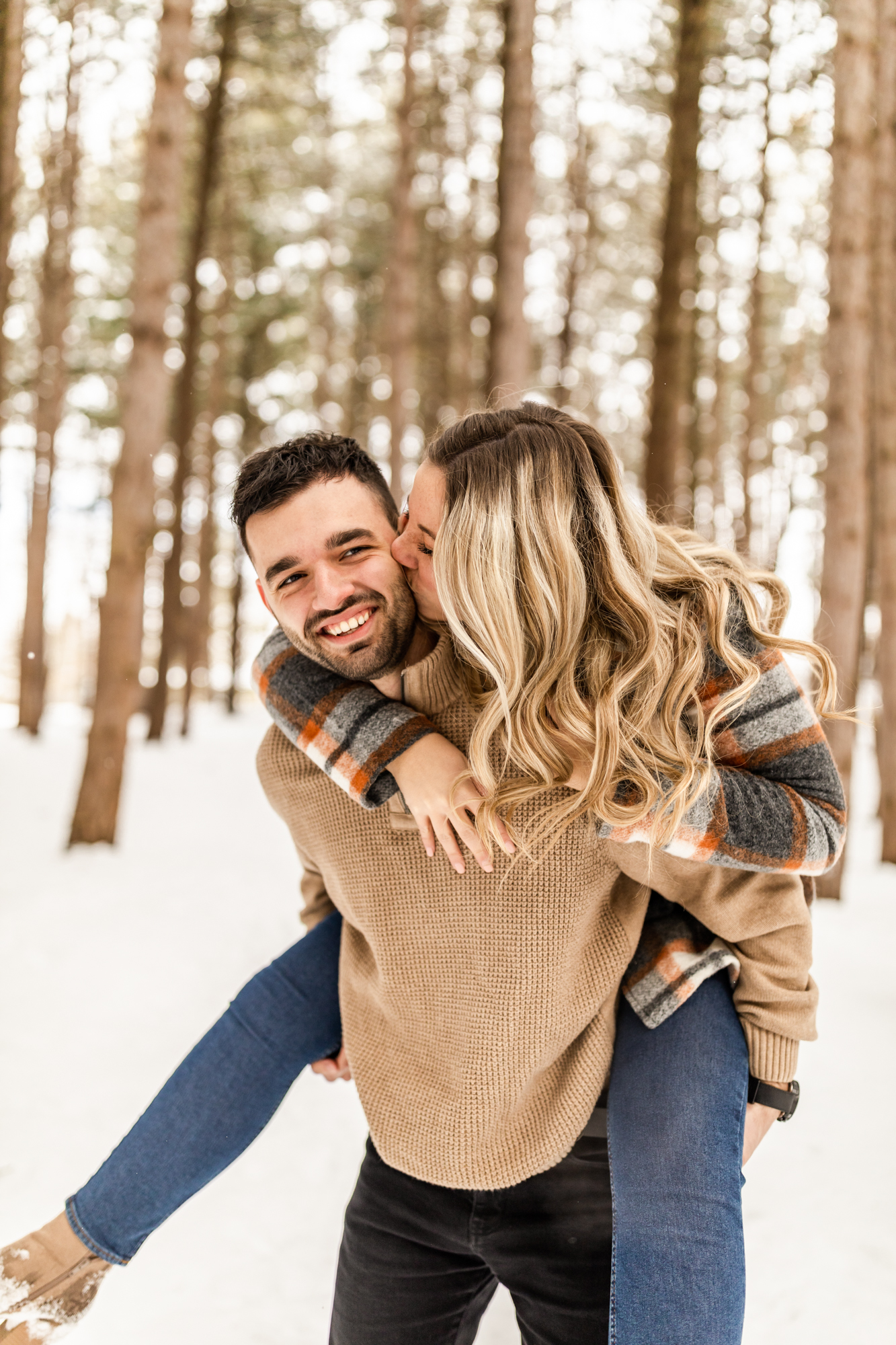 Man carrying woman on his back and smiling in engagement photos in the snow
