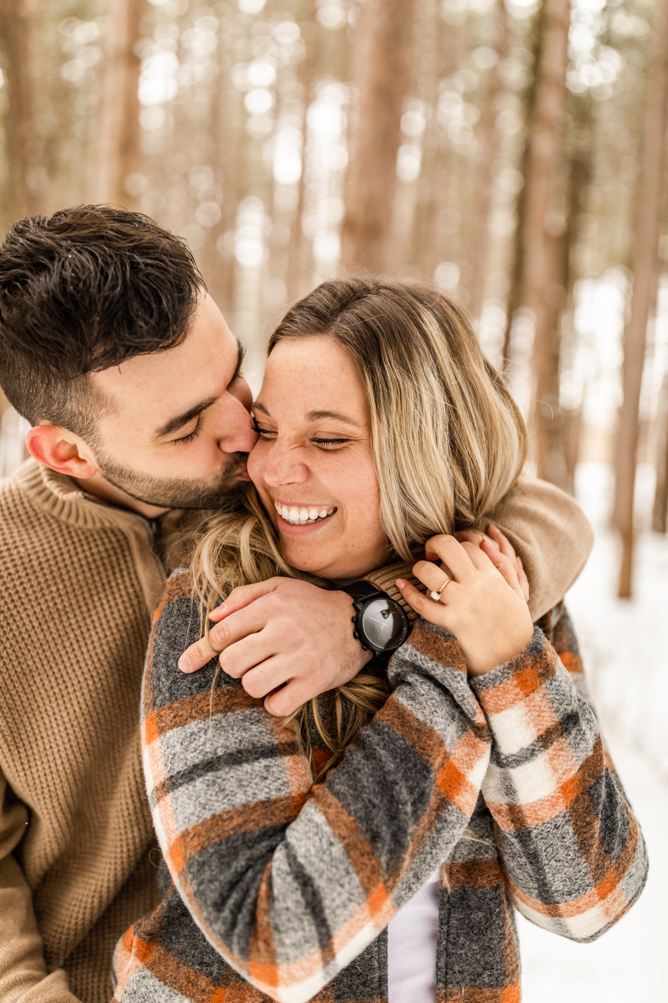 man kissing woman on cheek in snowy forest in Michigan