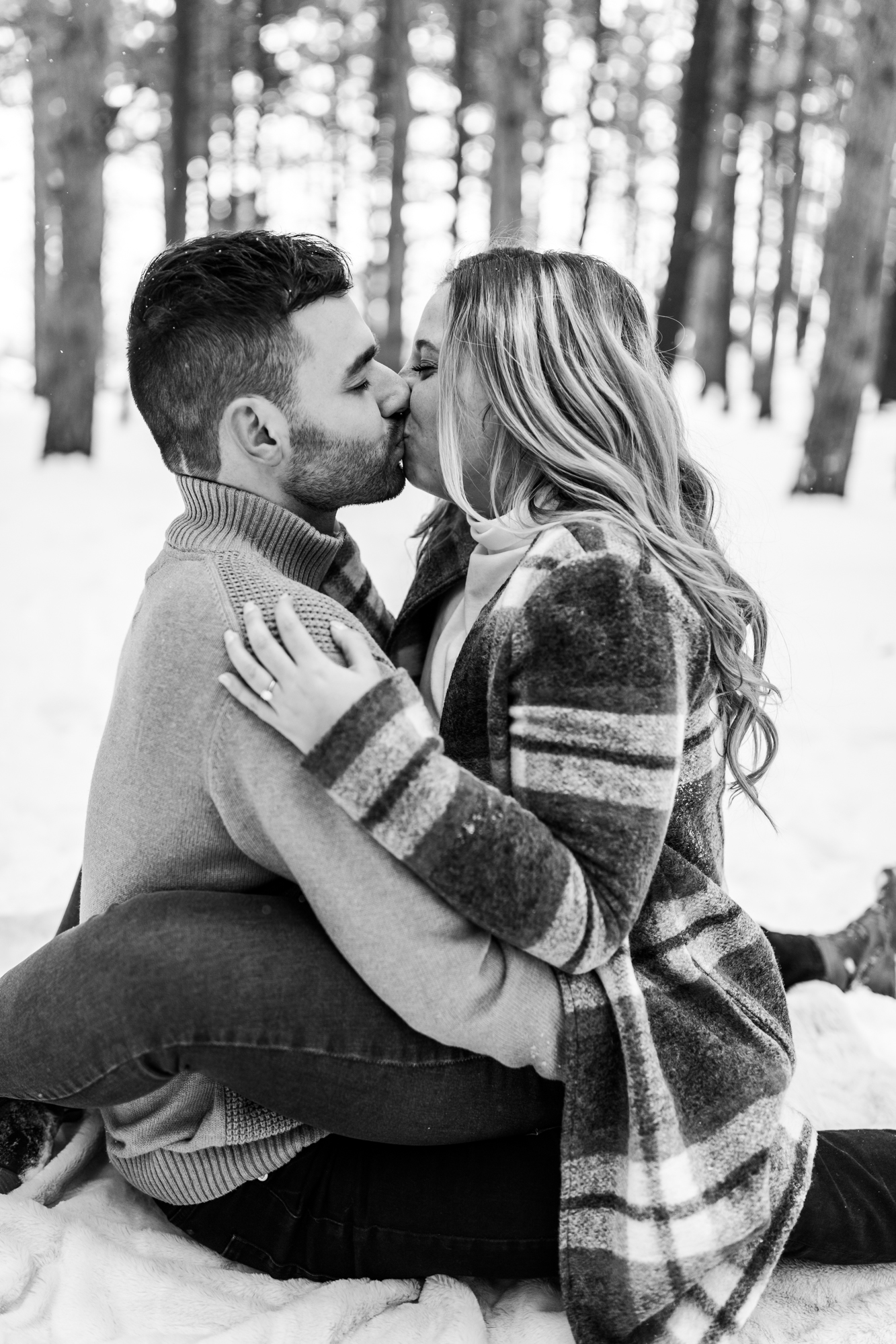 Couple sitting on blanket and kissing in snowy woods in Michigan