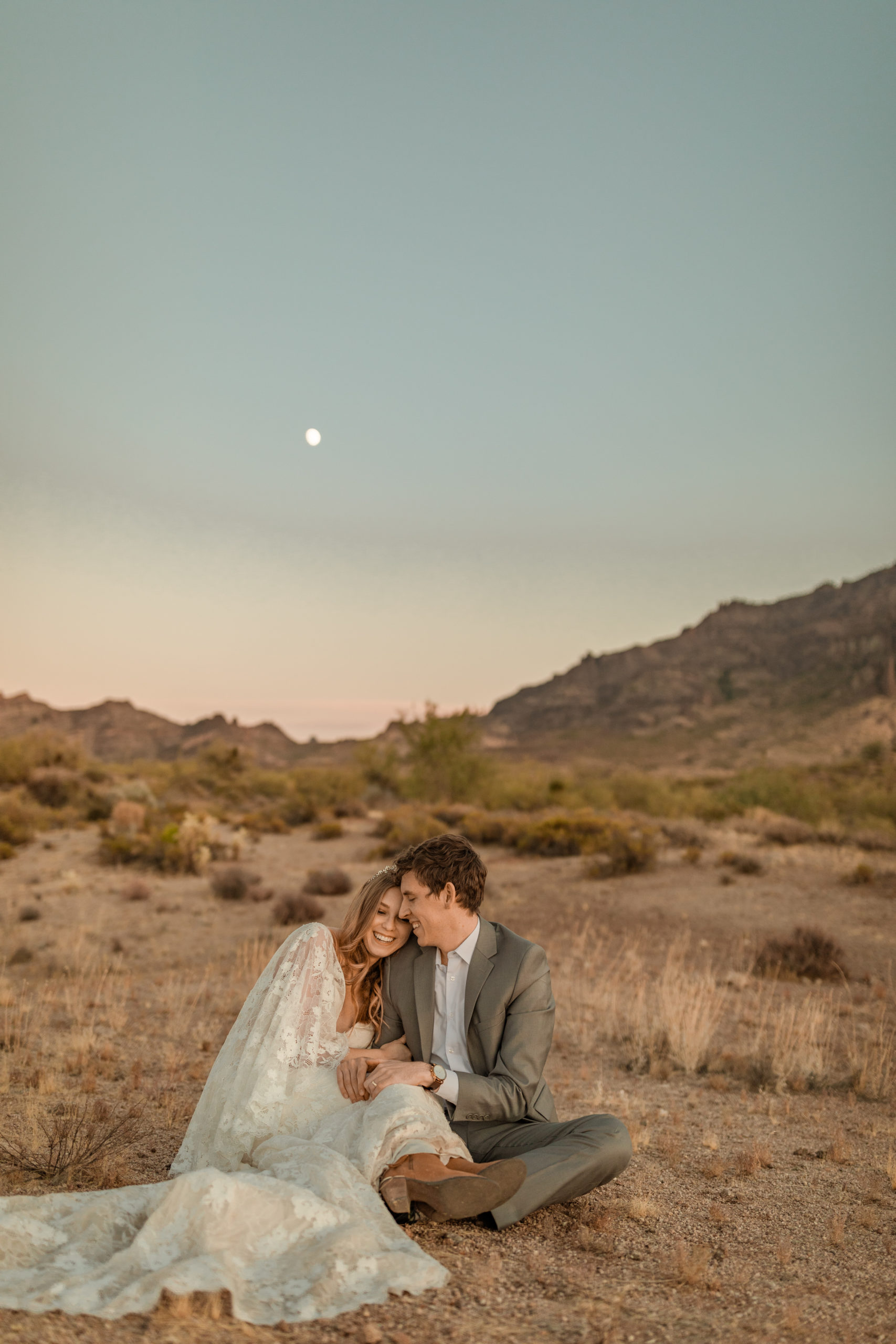 bride and groom sitting on the ground hugging candid wedding photos in Arizona