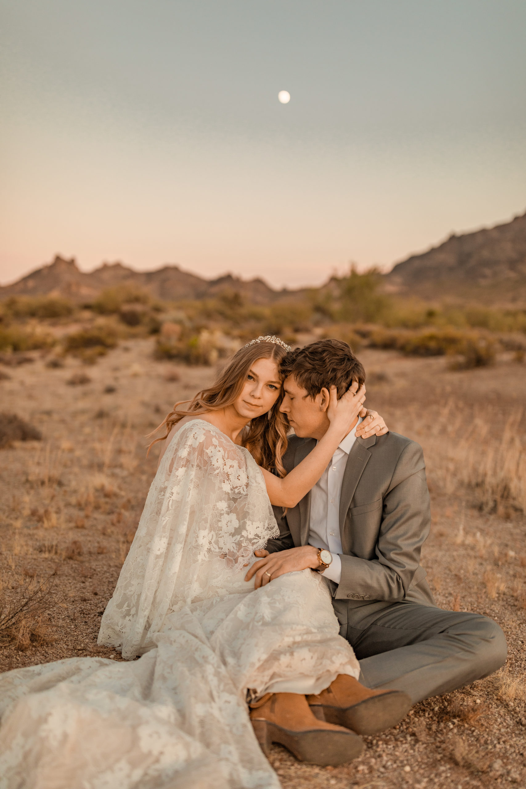boho bride and groom sitting on the ground hugging at elopement