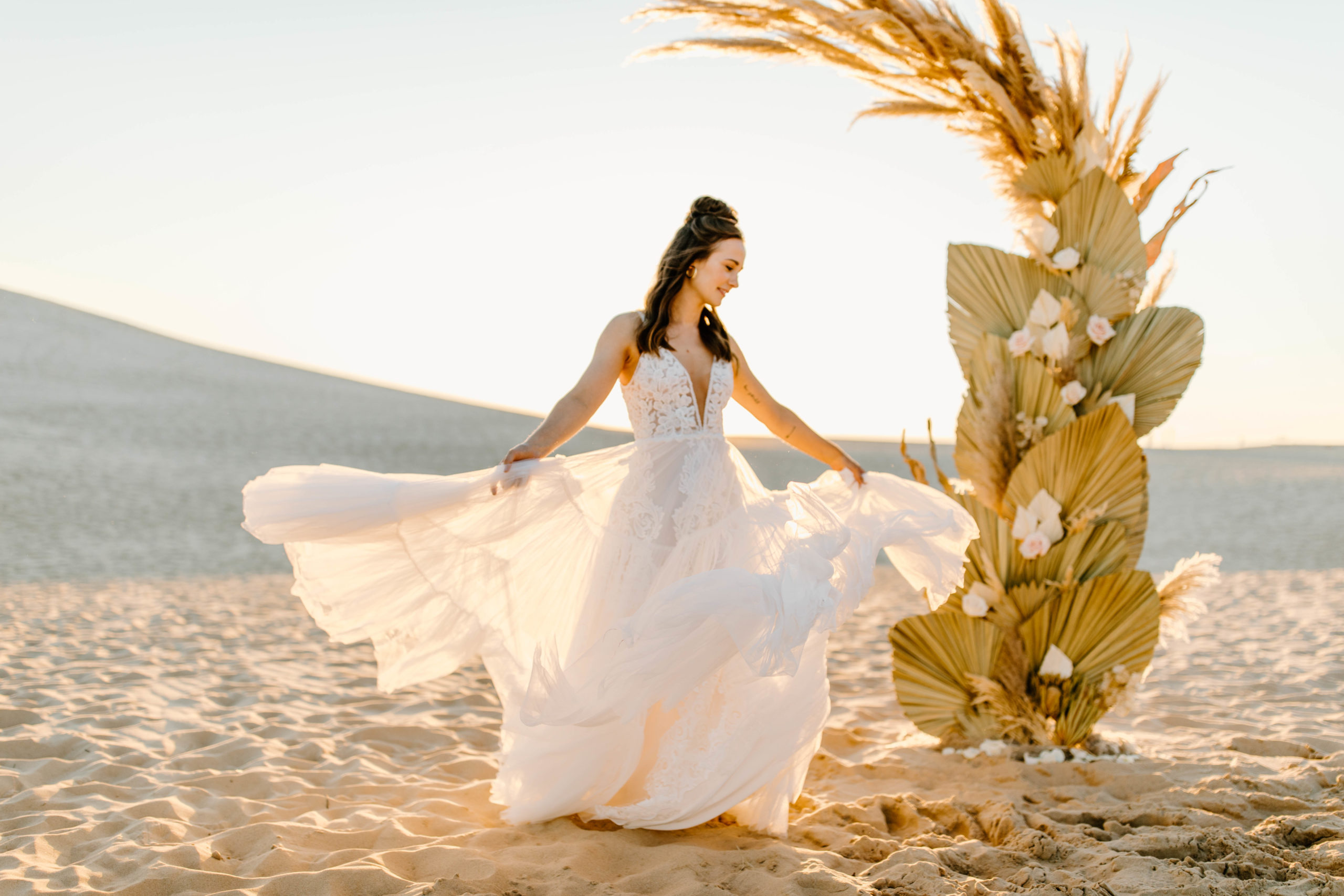 bride twirling in Sand Dunes in boho elopement wedding dress in front of Palms and Pampas Grass
