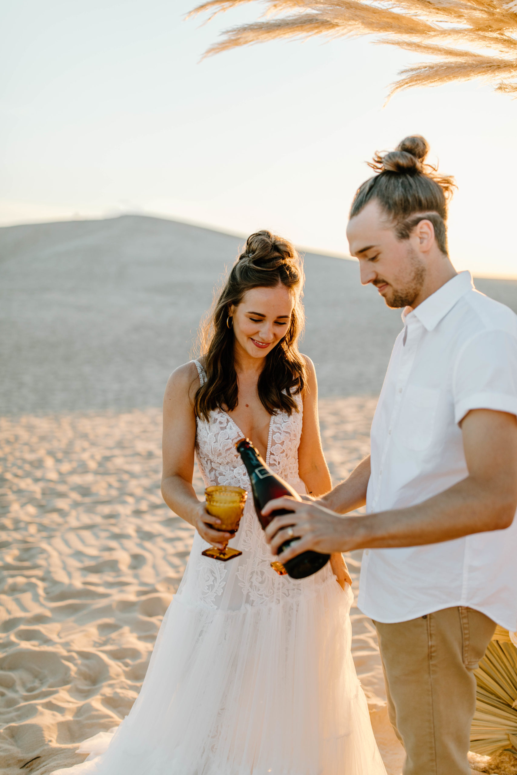 couple popping champagne at Sand Dune Elopement in front of Palms and Pampas Grass