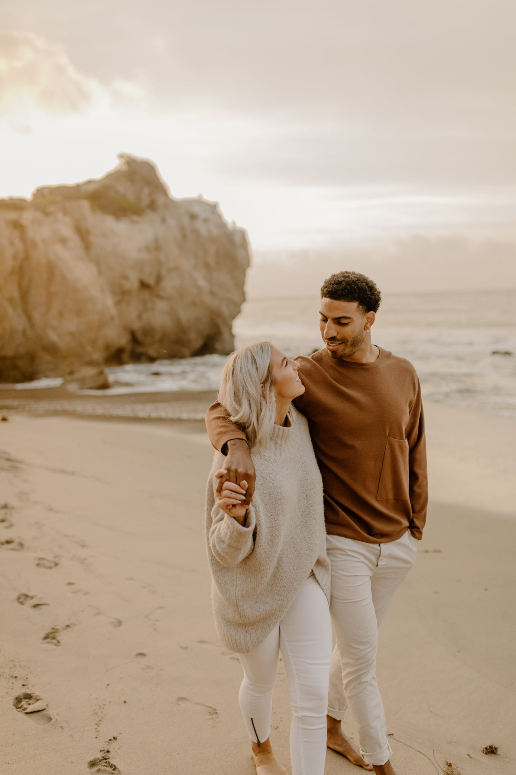 couple holding hands walking down beach in California for engagement photoshoot