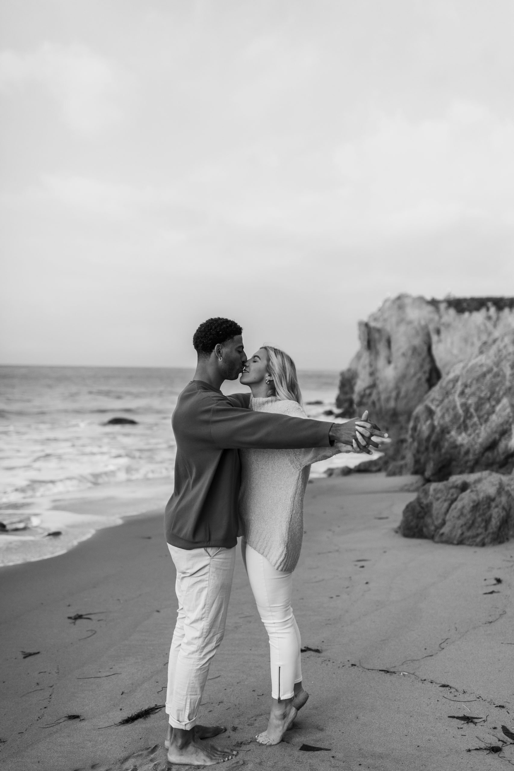 couple holding hands kissing on beach in California photoshoot