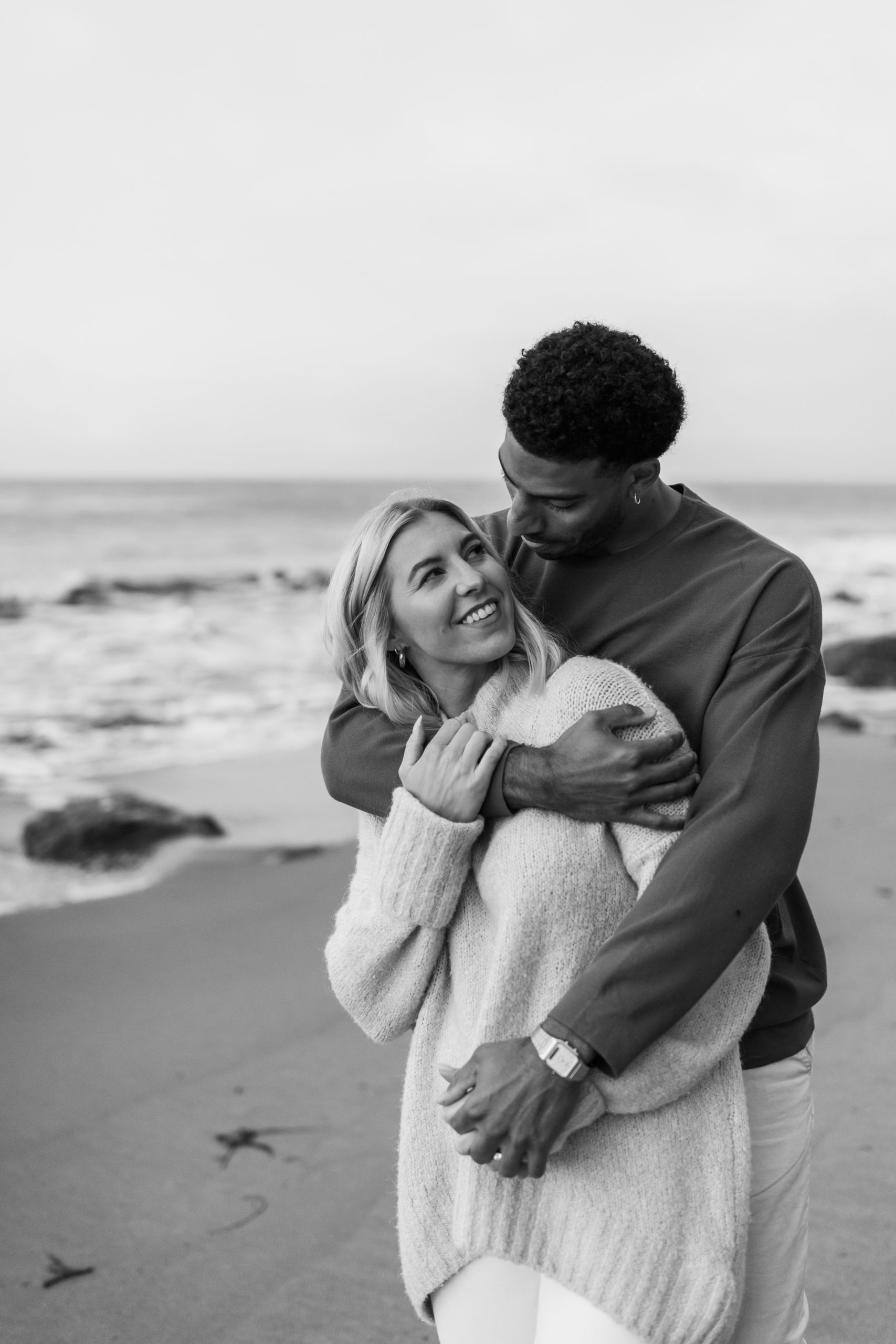 couple hugging on beach in California black and white engagement photos