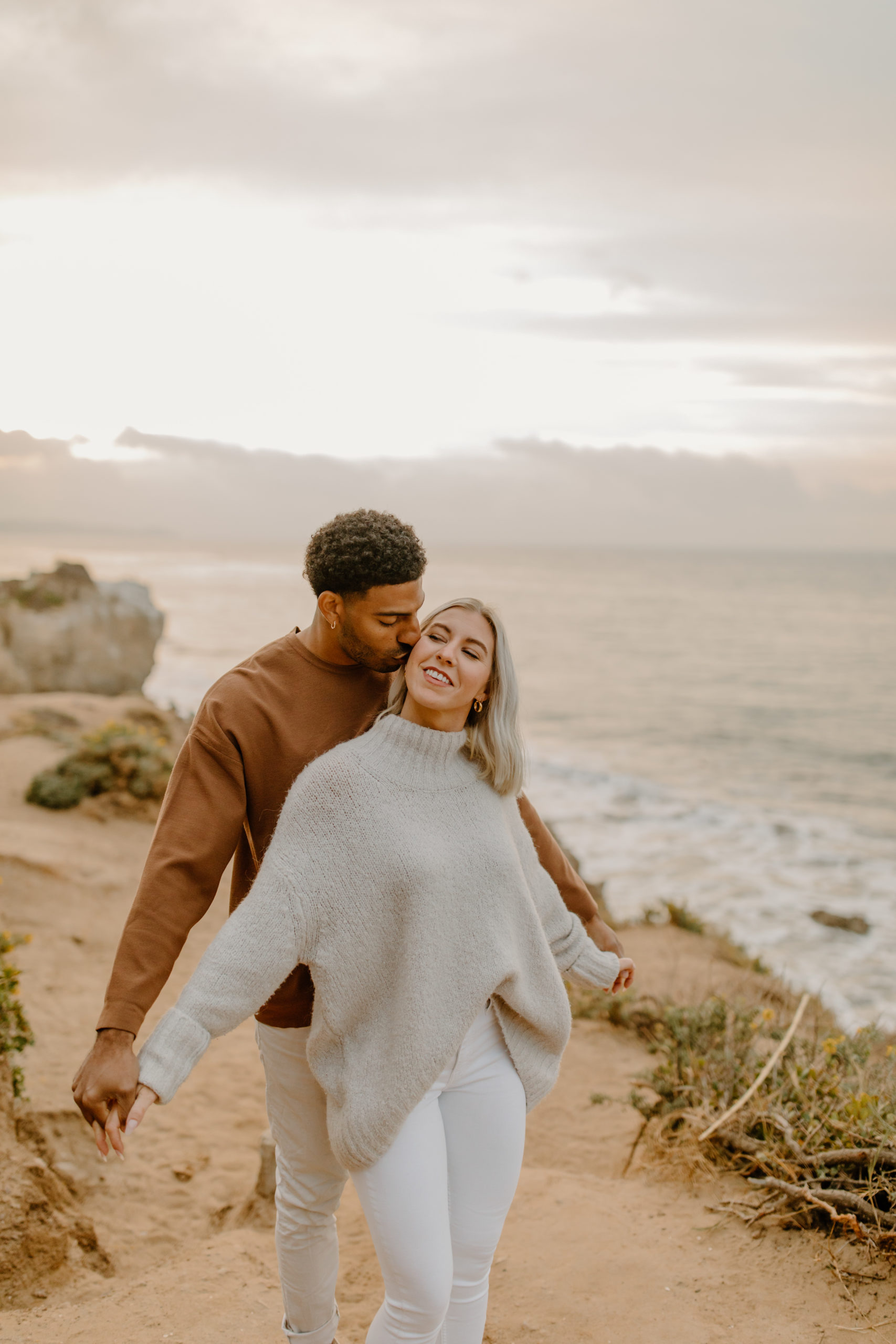 Candid natural engagement photos holding hands and kissing at Malibu beach in California