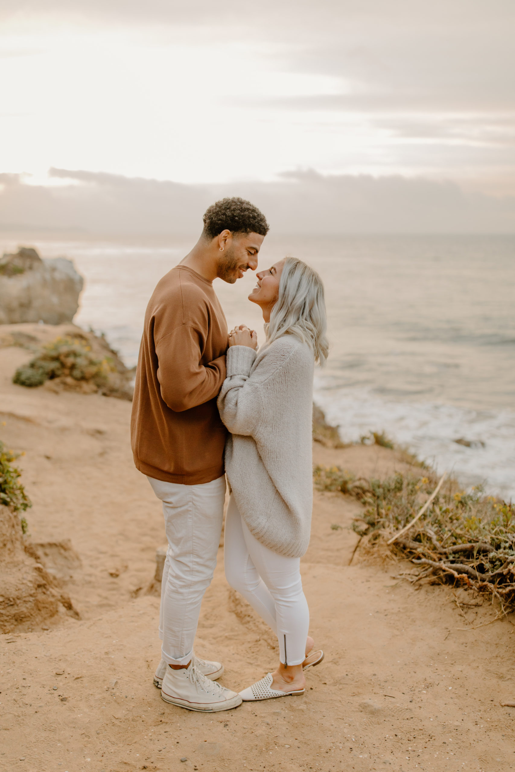 couple holding hands on top of cliff overlooking ocean in Malibu California