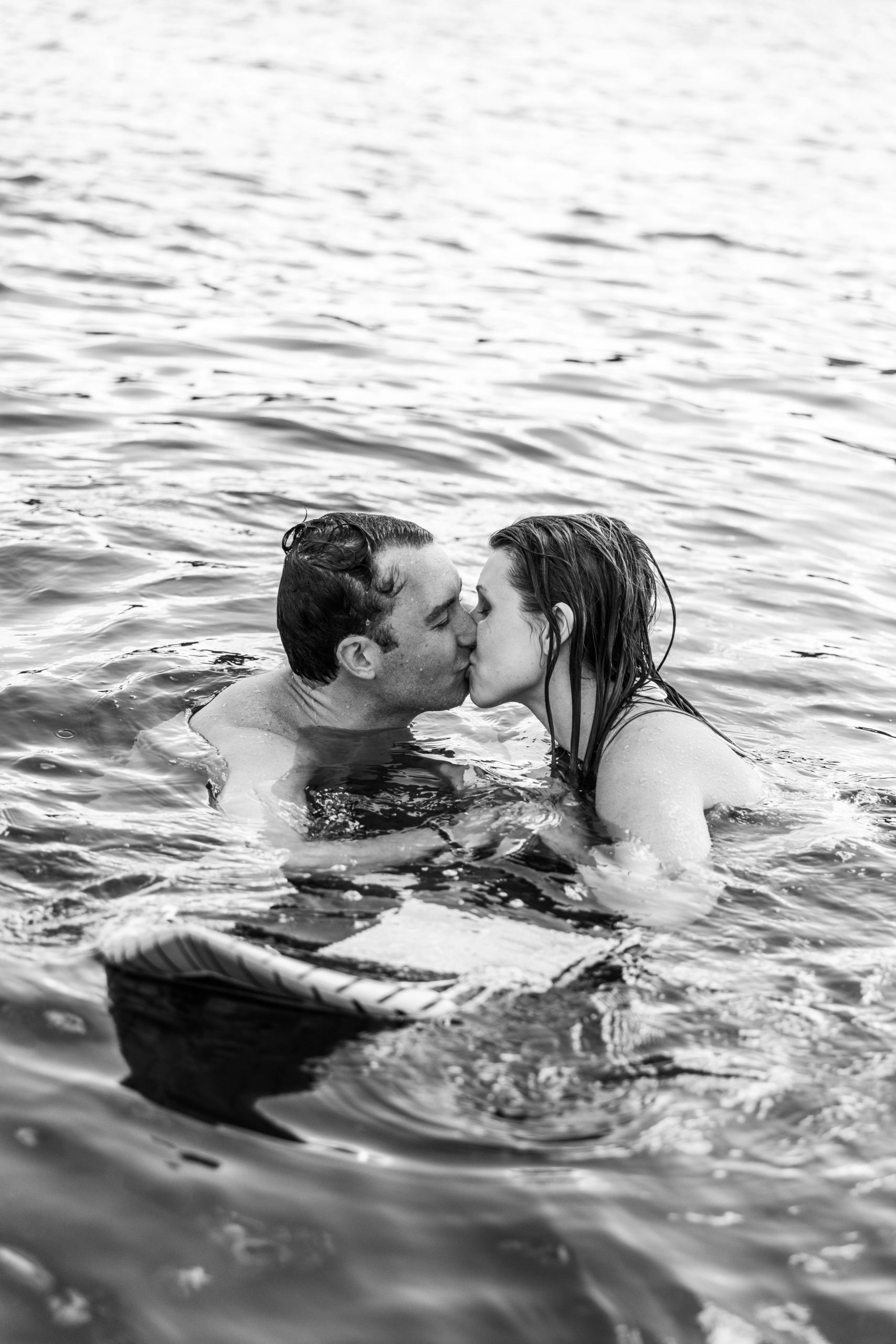 surfing lake michigan engagement photos couple in water with surfboard
