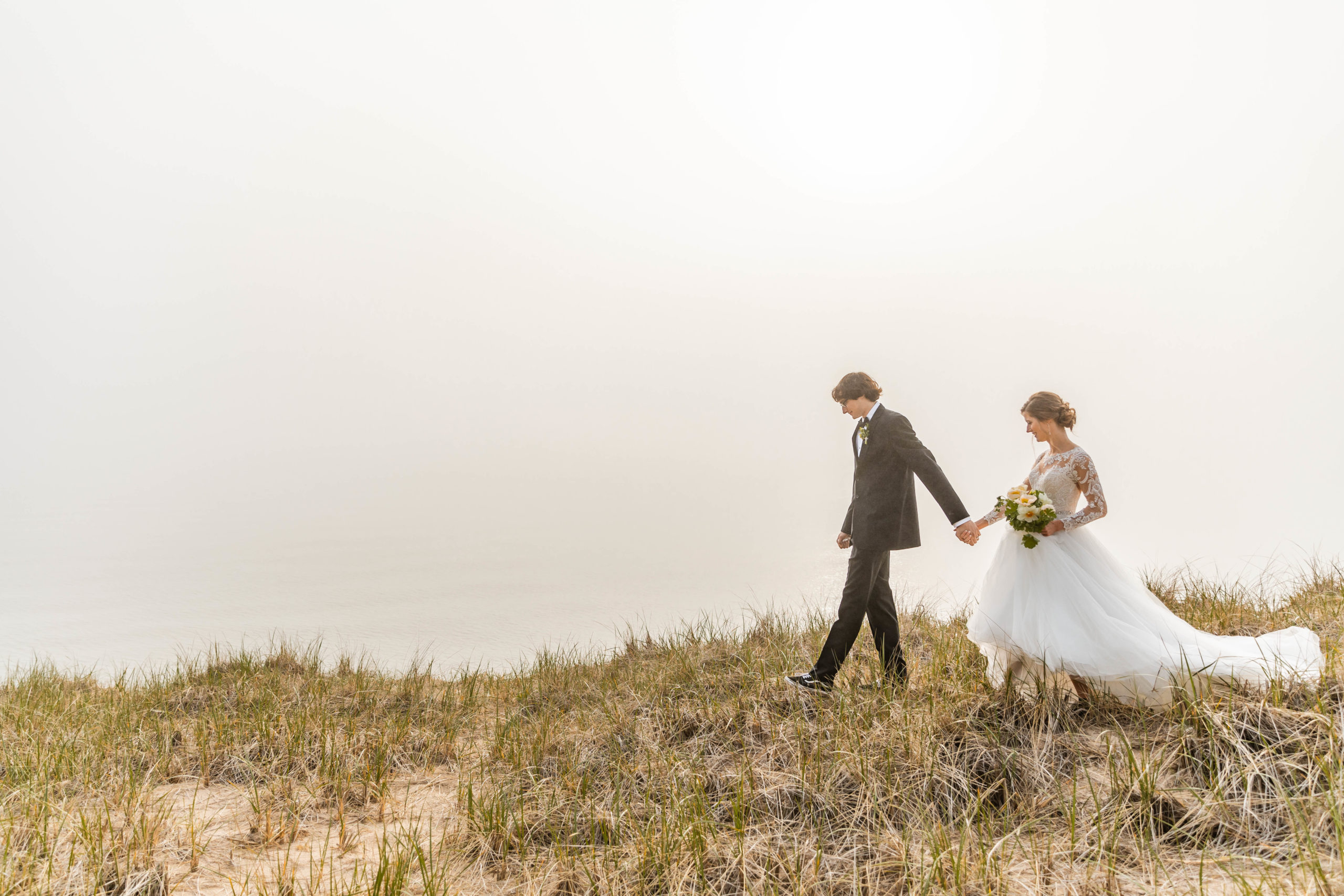 Bride and groom walking along sand dune overlooking lake michigan