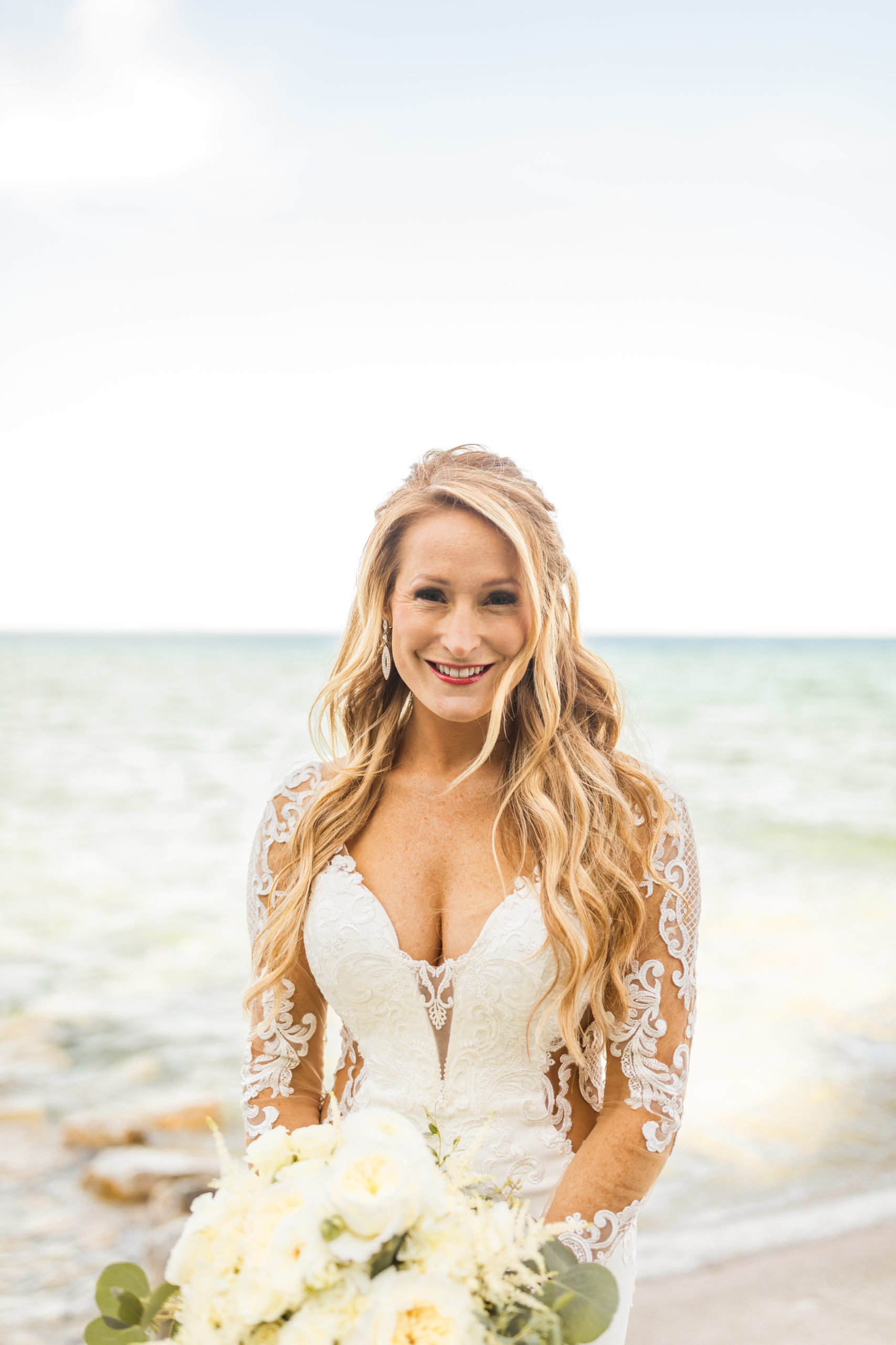 Bride holding bouquet smiling in front of Lake Michigan