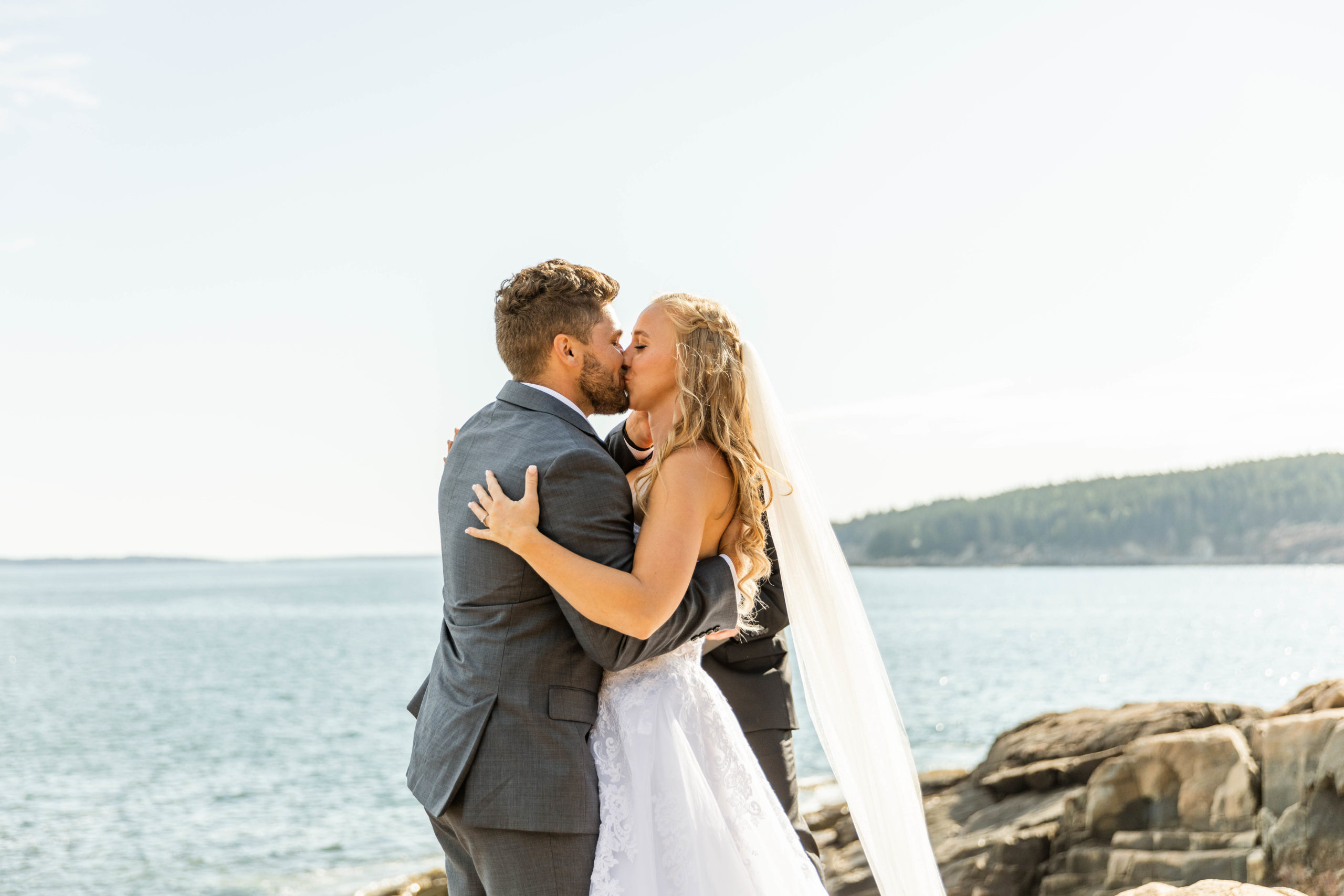 bride and groom kissing on bluff overlooking sea at Acadia National Park elopement