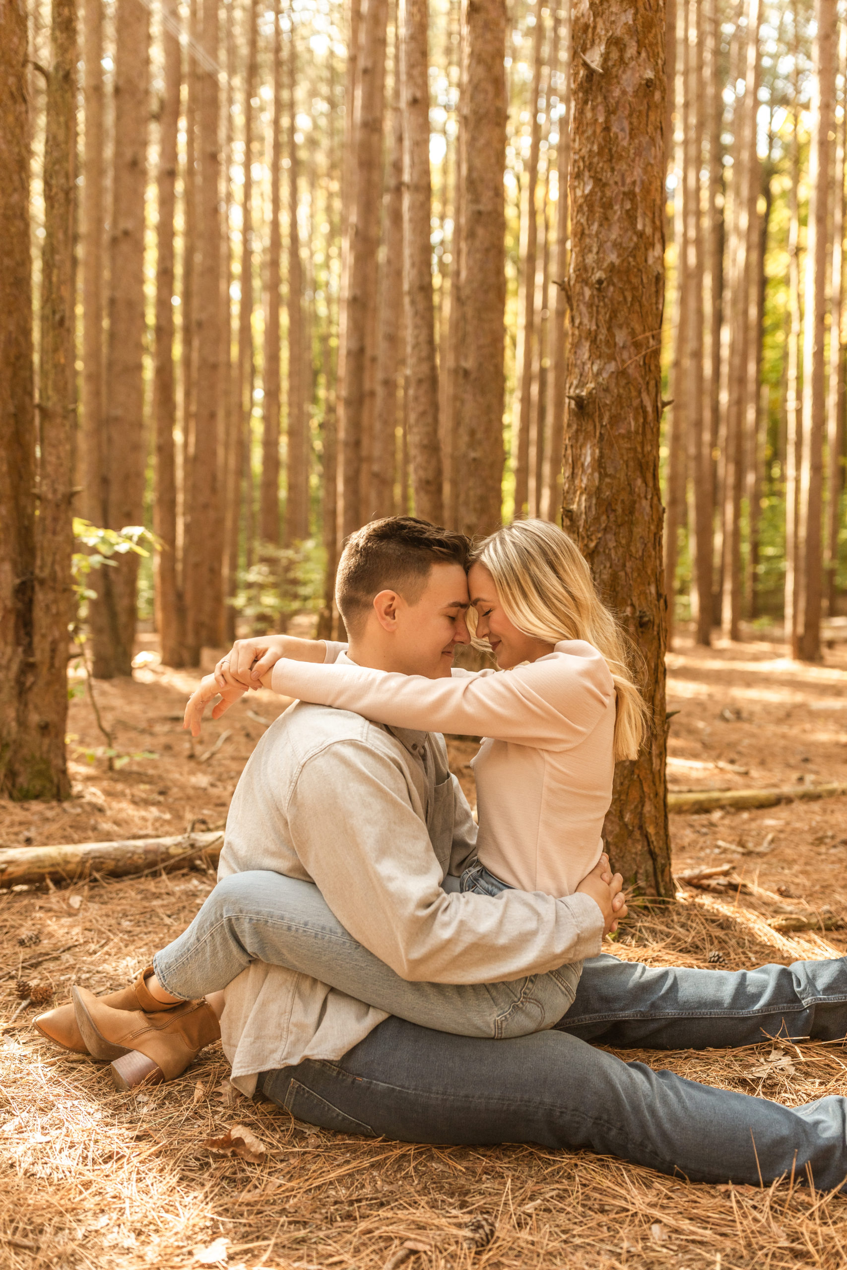 couple sitting on the ground hugging in a wooded forest in Michigan