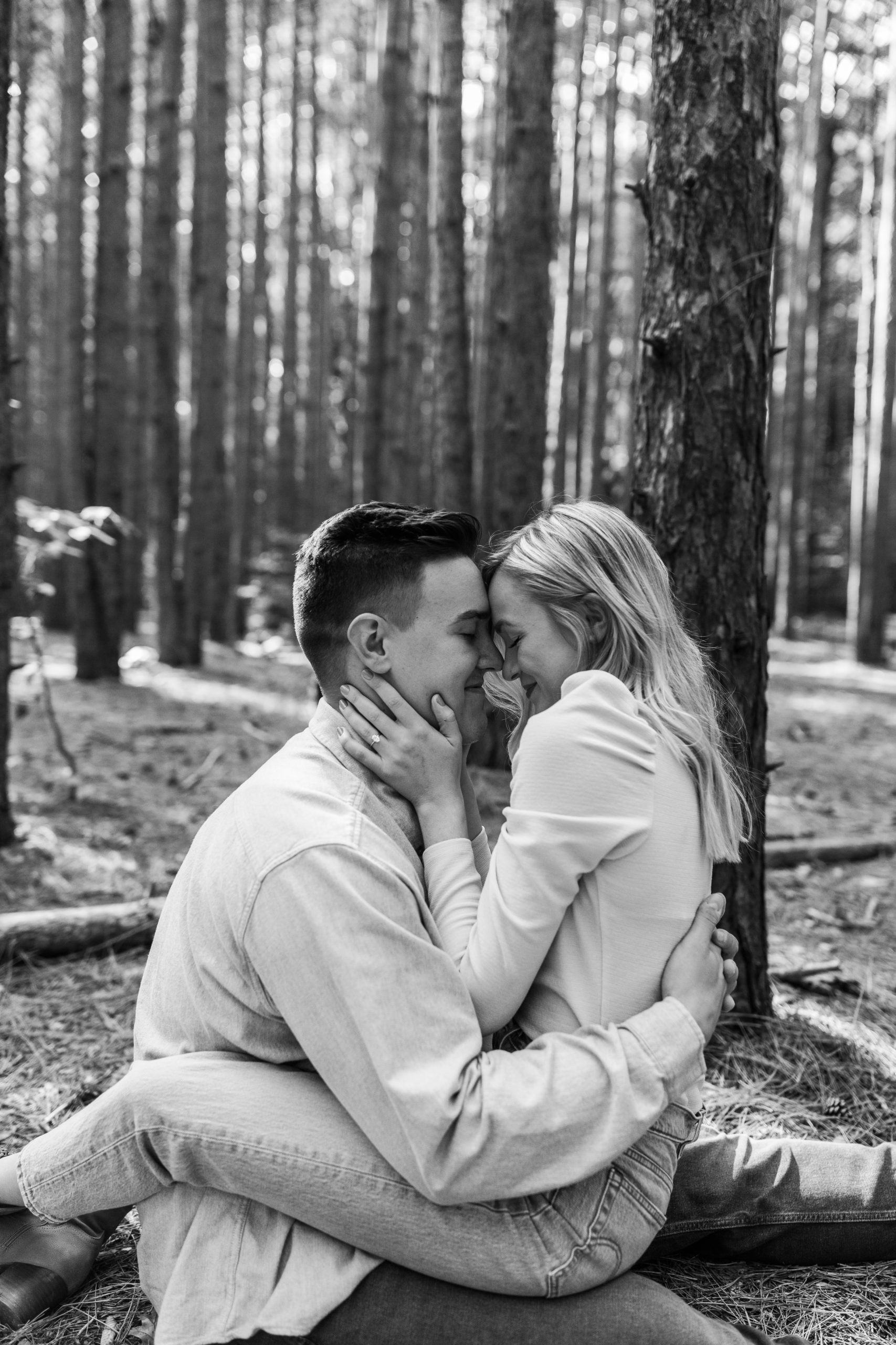 candid couple sitting on the ground hugging in a wooded forest