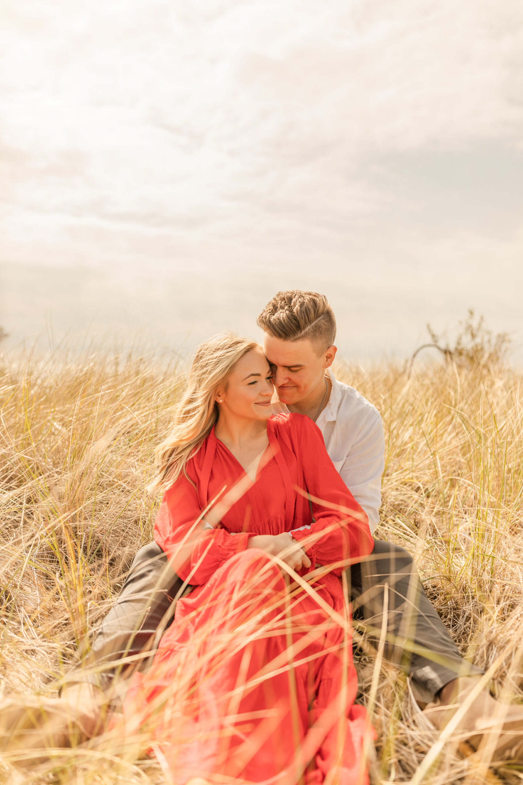 boho couple sitting in beach grass for Michigan engagement photos
