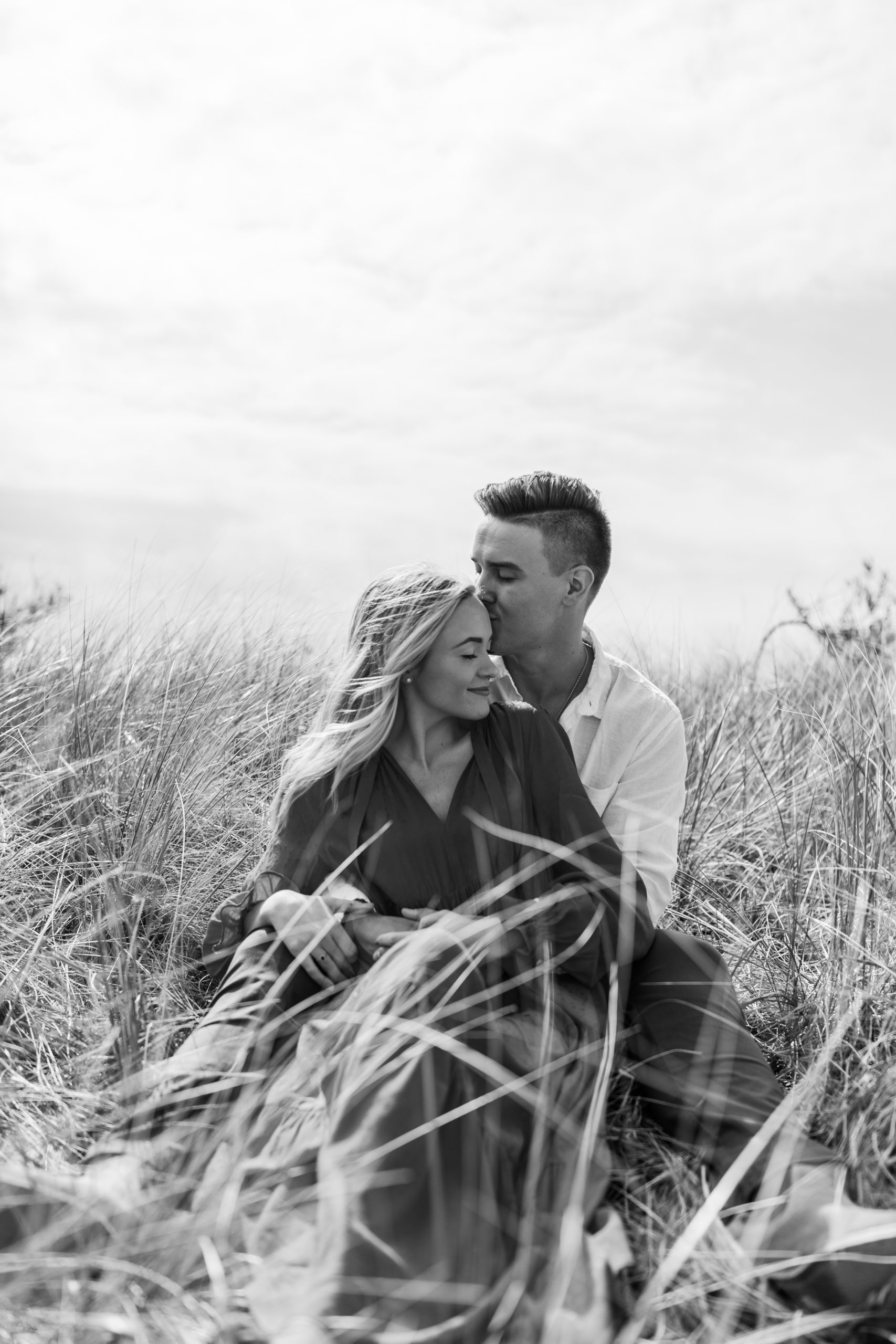 boho couple sitting in beach grass for candid engagement photos