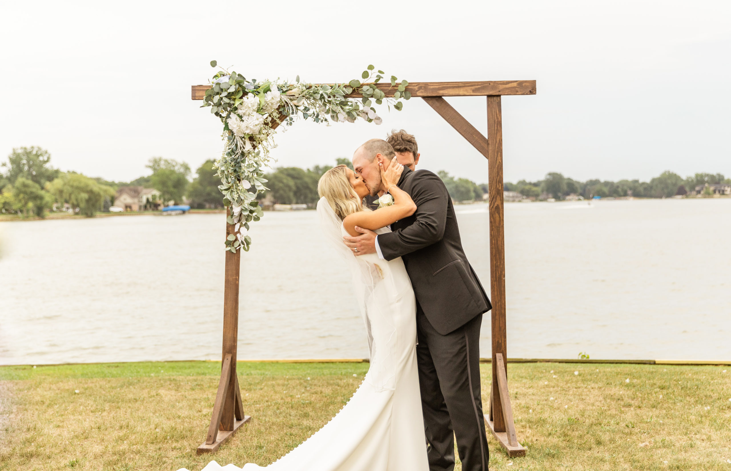 bride and groom kissing under ceremony arch in front of lake in Michigan