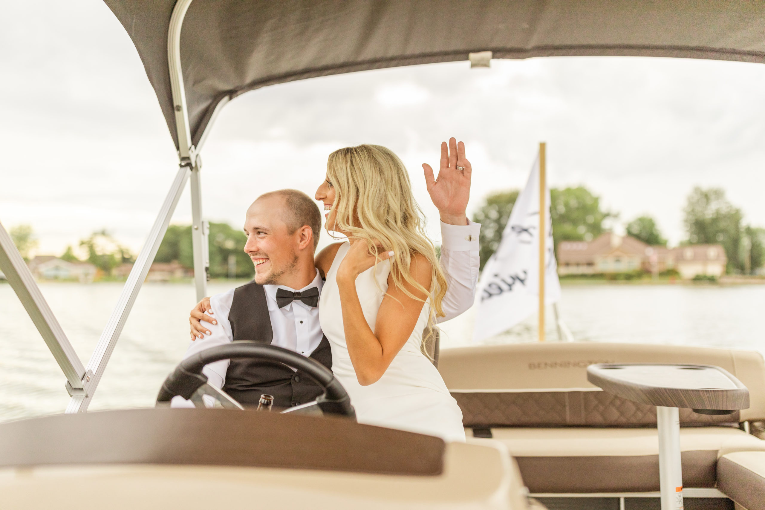 bride and groom waving from pontoon boat at lakefront wedding