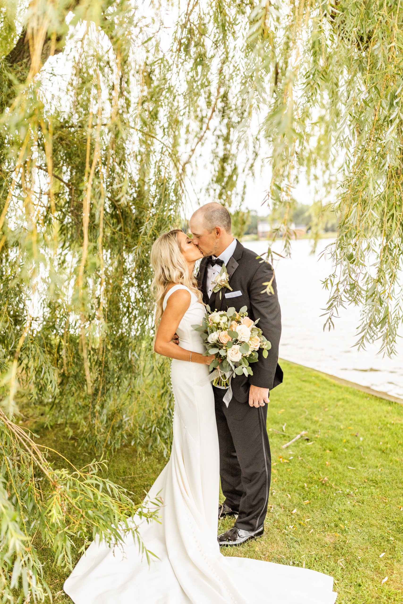 bride and groom kissing under lakefront willow tree wedding