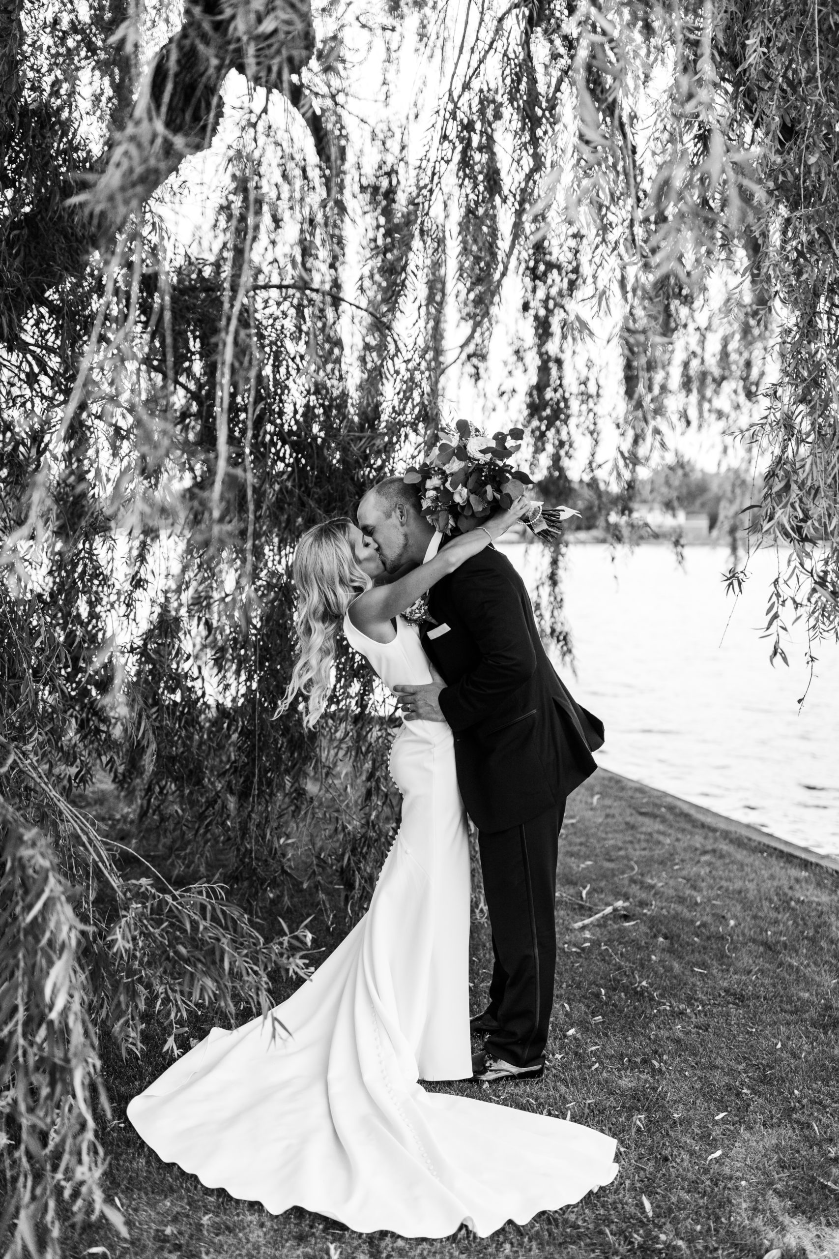 bride and groom kissing under lakefront willow tree in Michigan intimate wedding