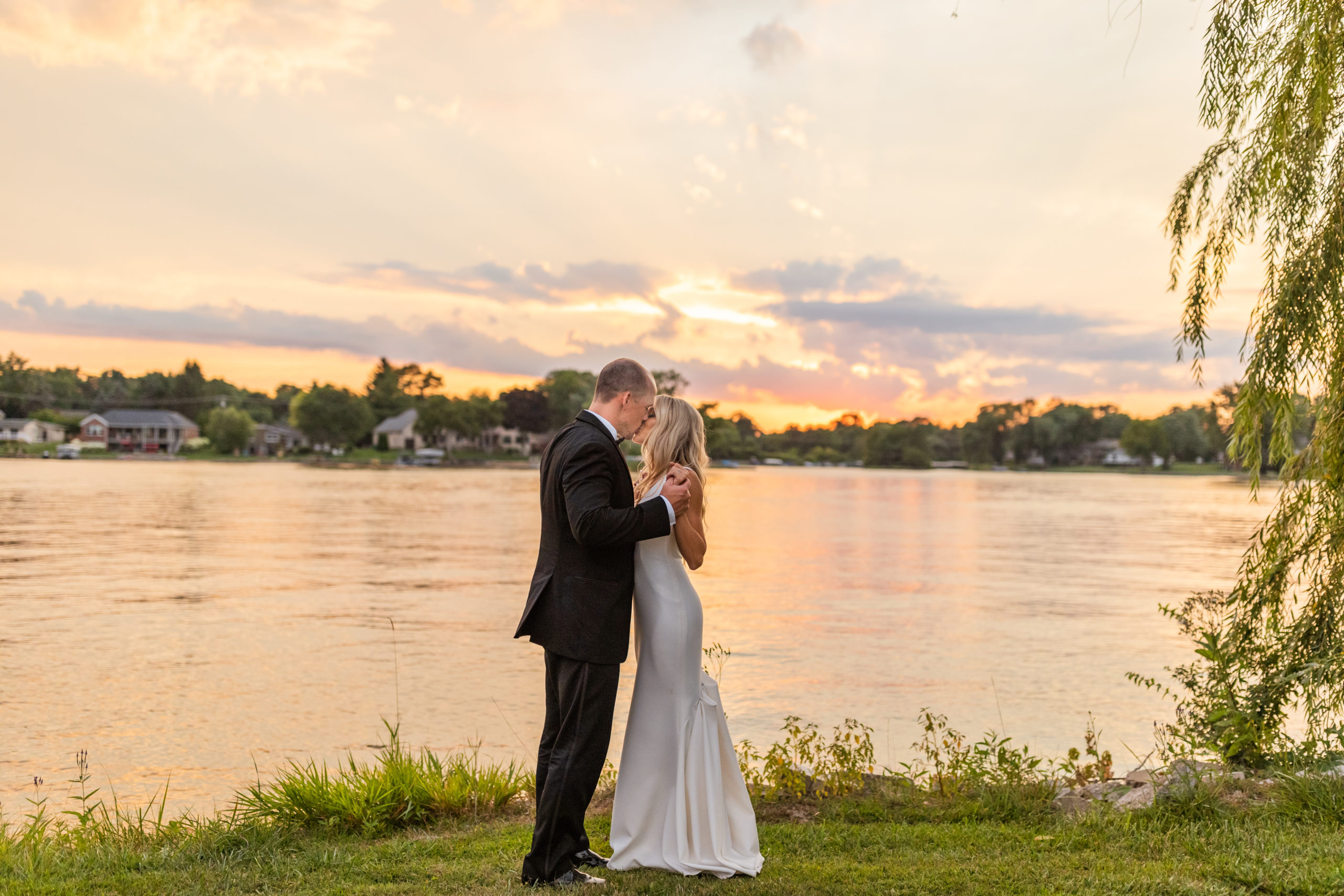 bride and groom kissing in front of lake at sunset in Michigan wedding