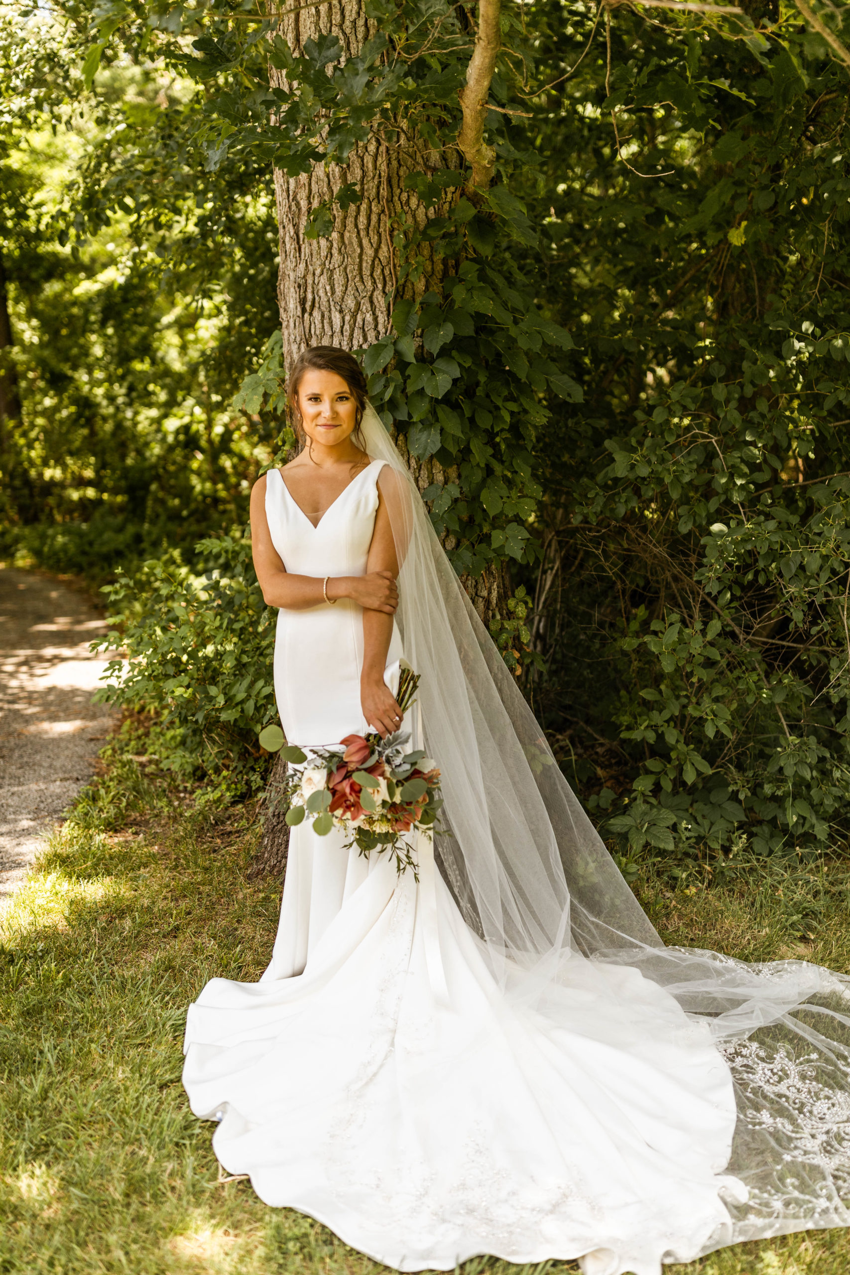 bride posing in front of tree with bouquet and long veil