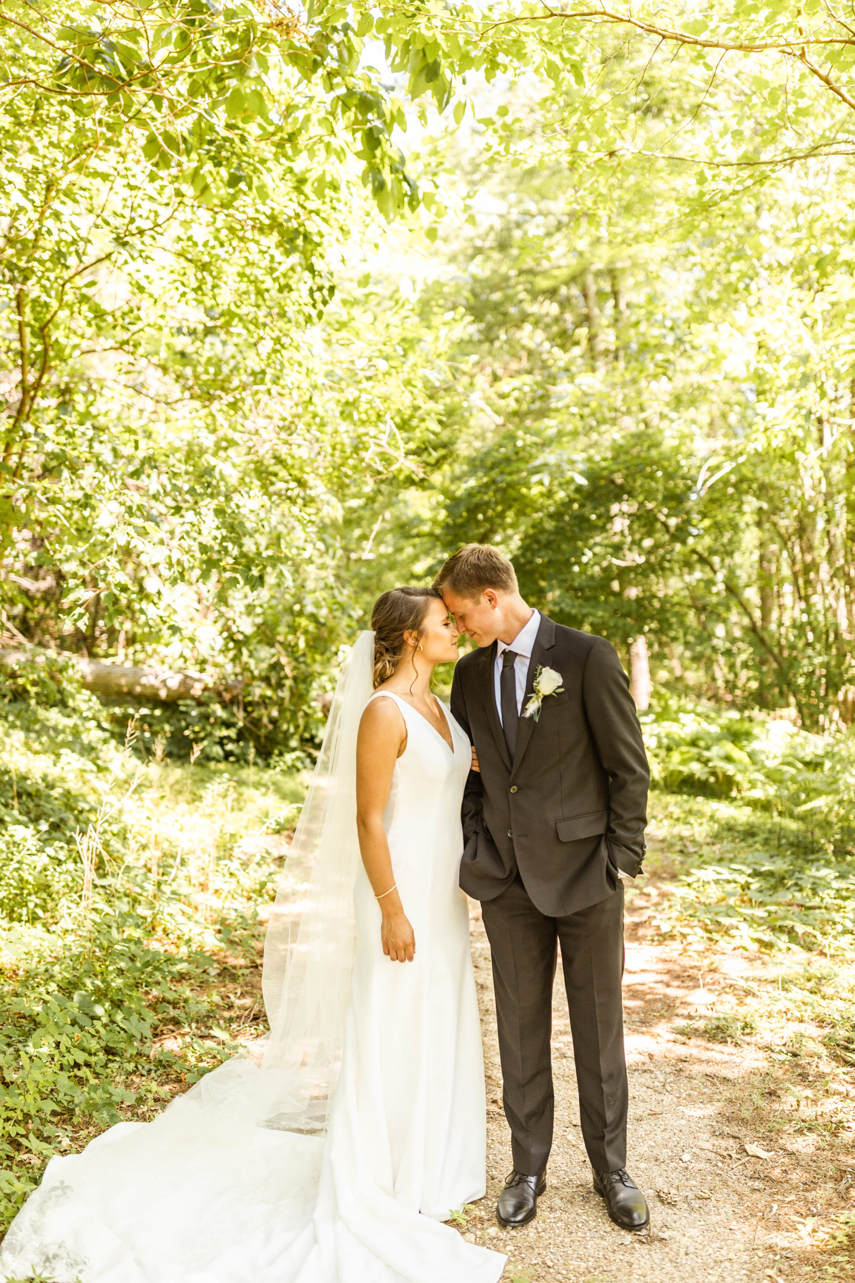 bride and groom standing together in wooded trail