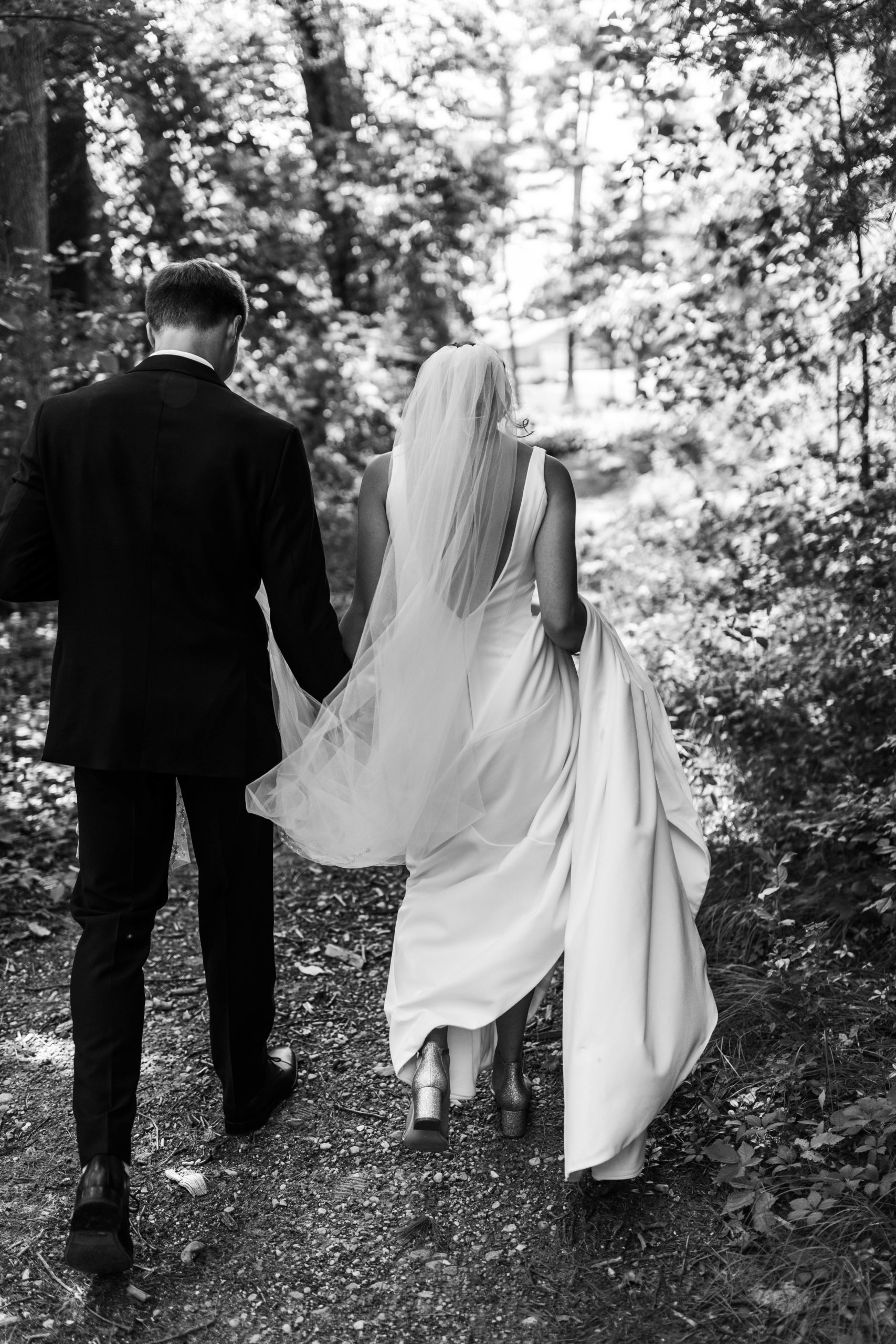 bride and groom holding hands walking down wooded trail