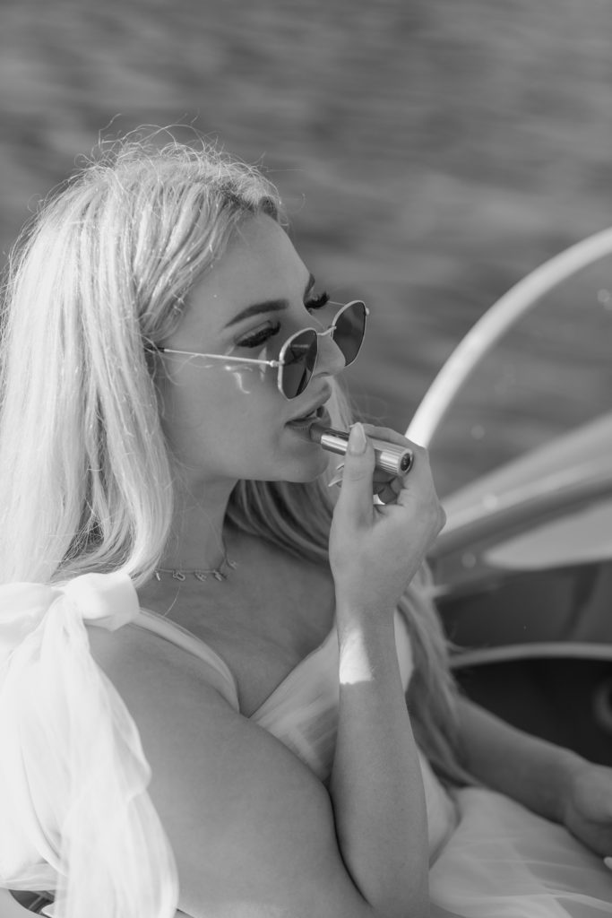 Bride applying lipstick with sunglasses and lipstick in wedding dress